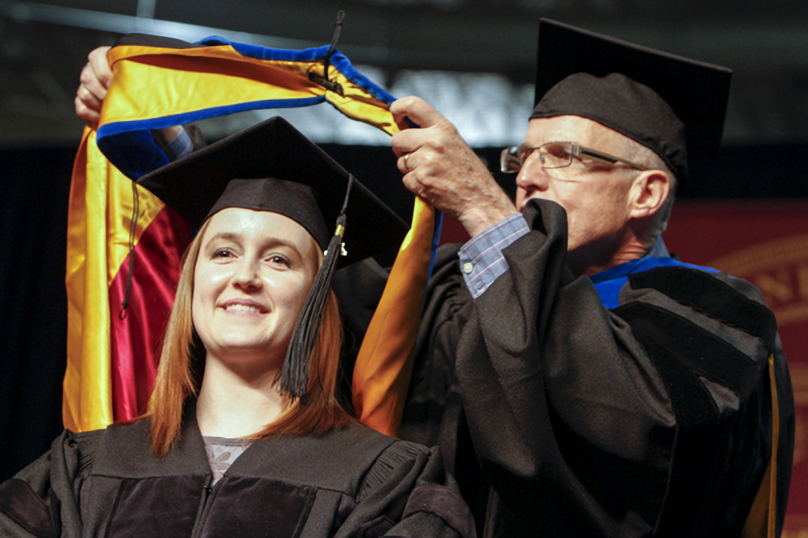 A master's degree student is receiving her hood from a faculty member.